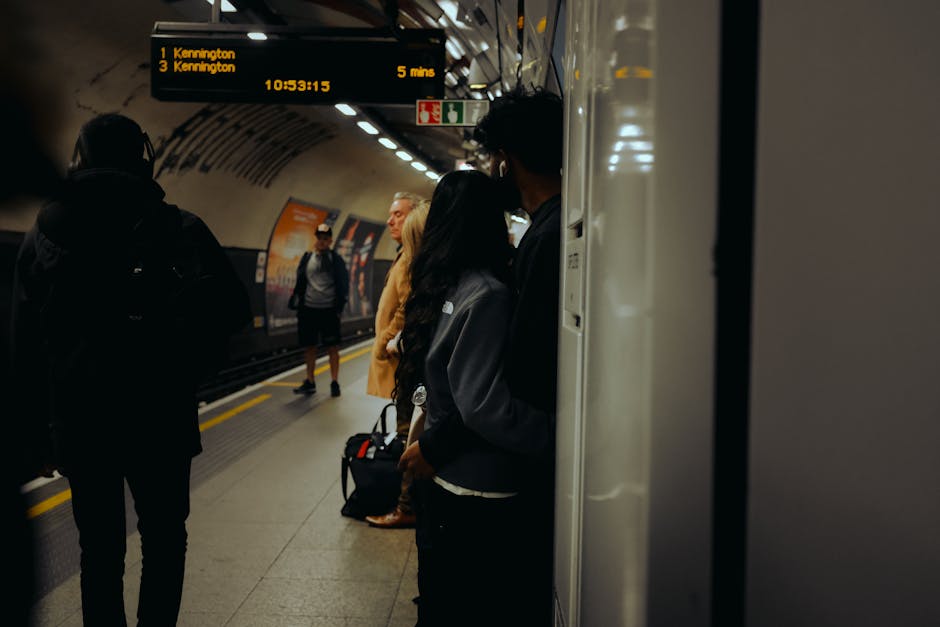 A view of Finsbury Park railway station platform with a metal roof overhead and multiple benches arranged along the platform. The platform surface is clean and well-maintained, with visible tactile paving at the edge. A sign indicating 'Finsbury Park' is suspended from the ceiling, and there are a few passengers sitting and waiting on the benches. The station's brick buildings and additional signage are visible in the background. The lighting is natural, suggesting daytime, and the overall scene reflects a tidy, hygienic public transport environment. Cleaner Kennington specialises in surface and deep cleaning, ensuring high standards of hygiene in busy areas like train stations, as seen in this well-kept platform picture.