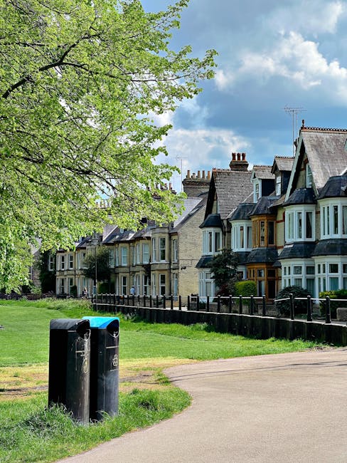 A row of traditional Victorian-style terraced houses with bay windows and slate roofs, situated along a green residential street in Kennington. In the foreground, two black rubbish bins are positioned